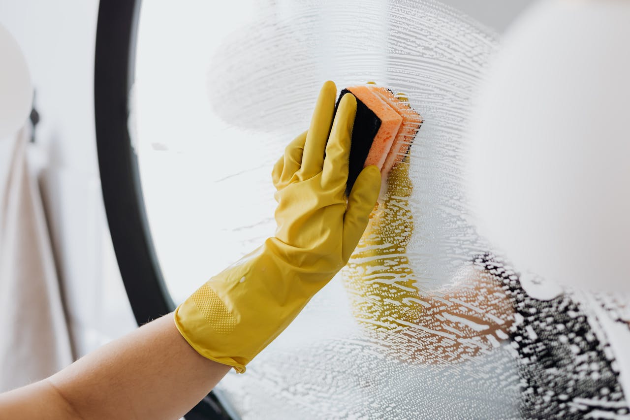 ours-journey Anonymous person in yellow rubber gloves using simple sponge for cleaning mirror in bathroom